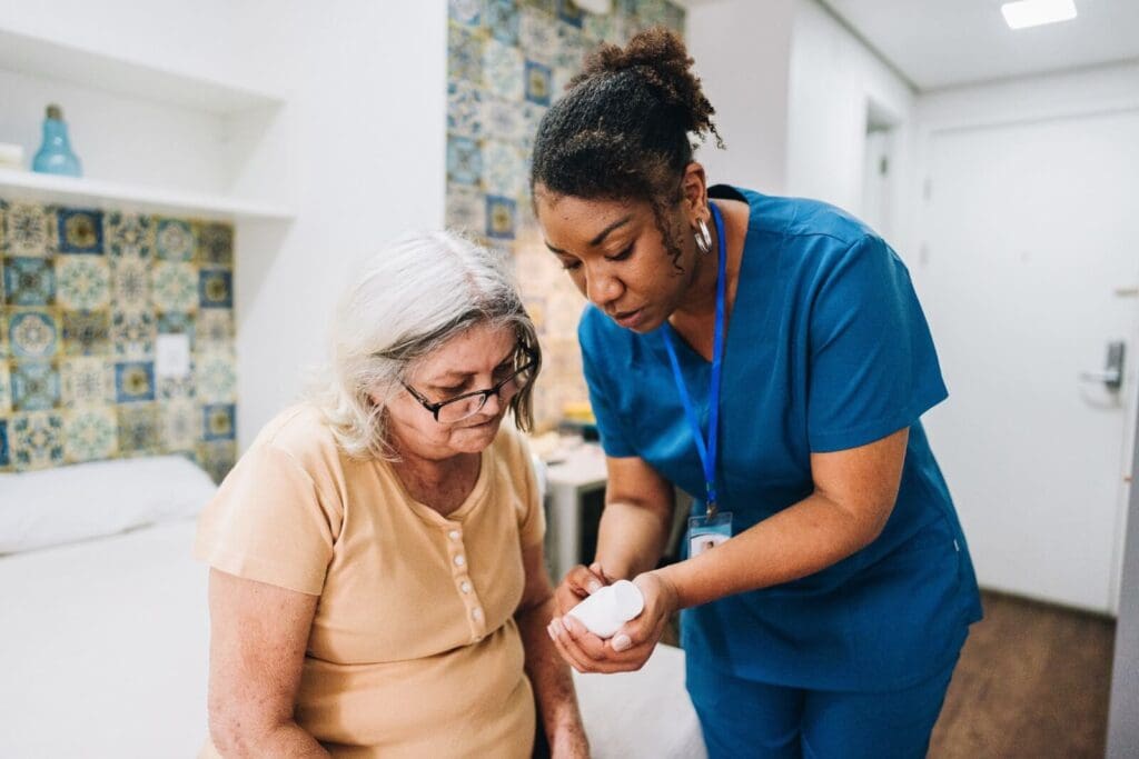 Nurse helps elderly woman take medication in bedroom