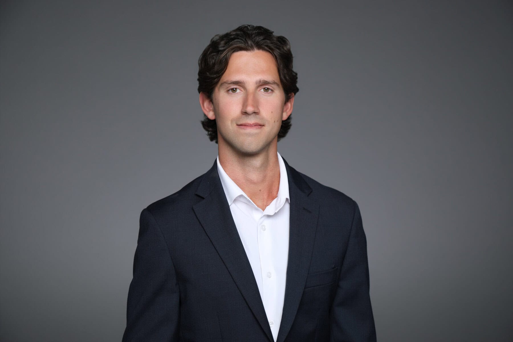 Professional portrait of Jordan Vetrone in a suit against a gray background.